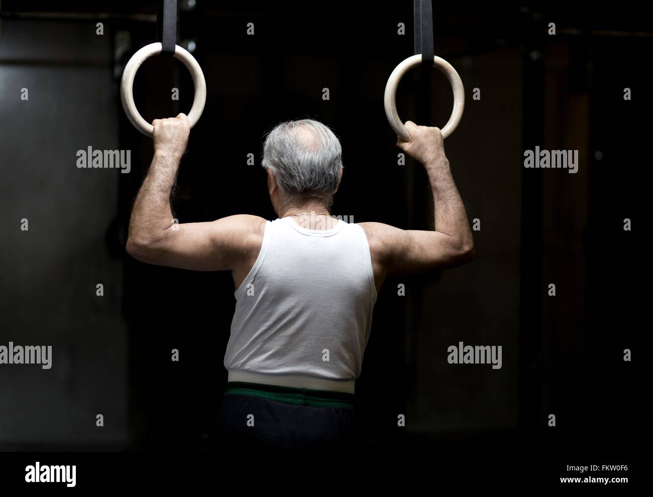 Rear view of senior man holding gym rings in dark gym Stock Photo