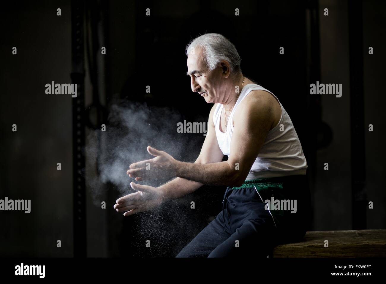 Senior man sitting chalking hands in dark gym Stock Photo