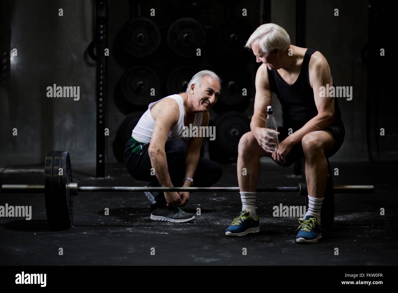 Senior men chatting and tying trainer laces in dark gym Stock Photo