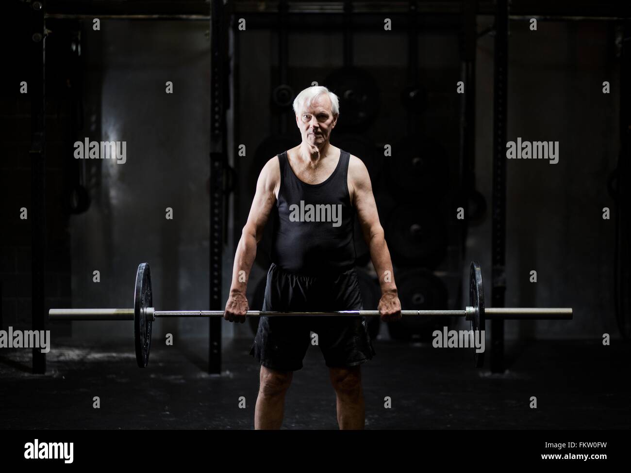 Senior man weightlifting barbell in dark gym Stock Photo