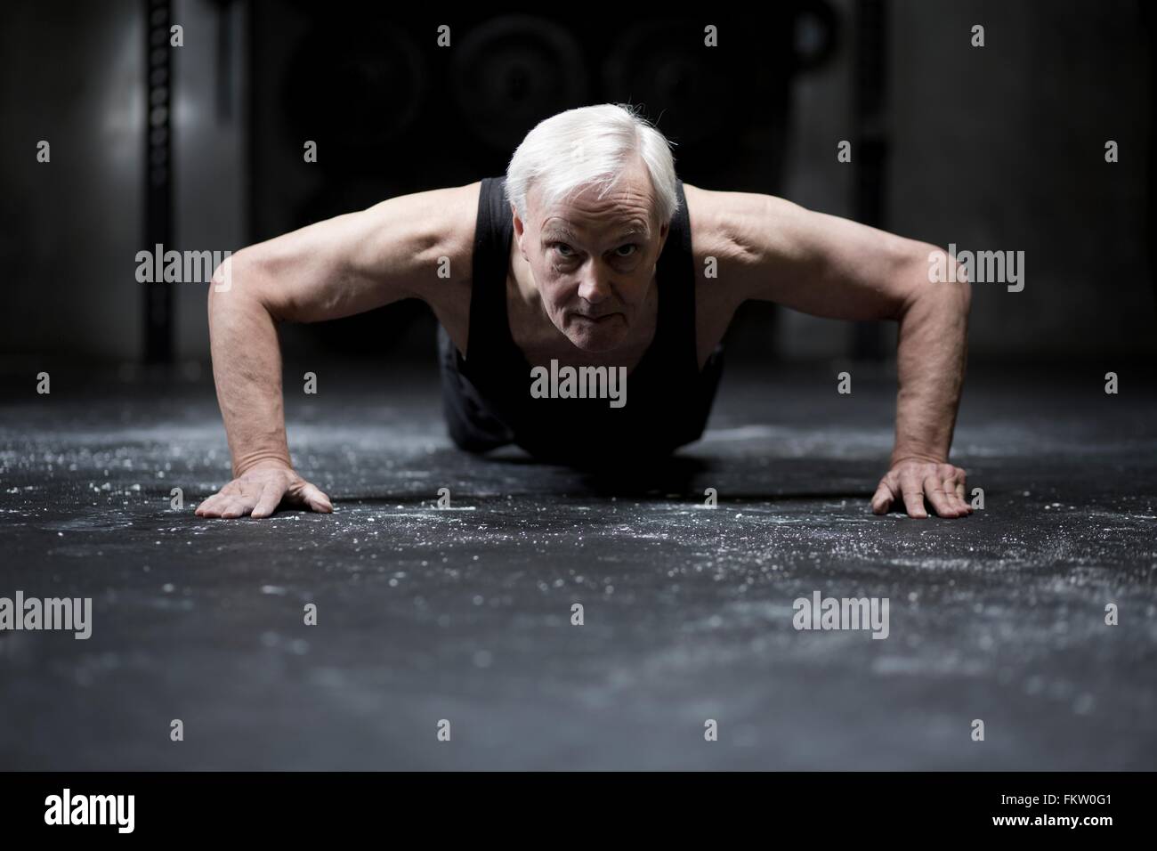 Surface level view of senior man doing push ups in dark gym Stock Photo