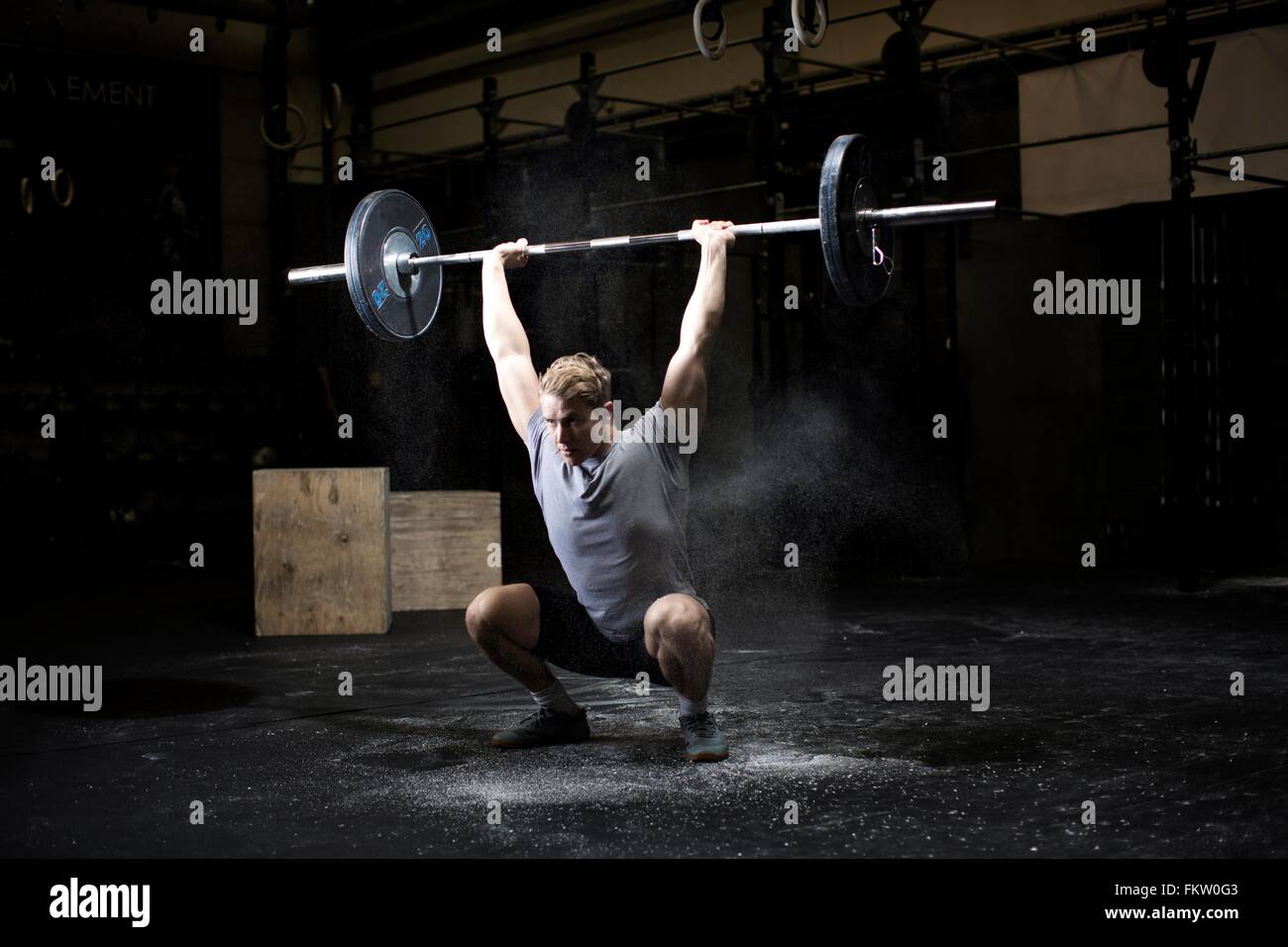 Young man weightlifting barbell in dark gym Stock Photo