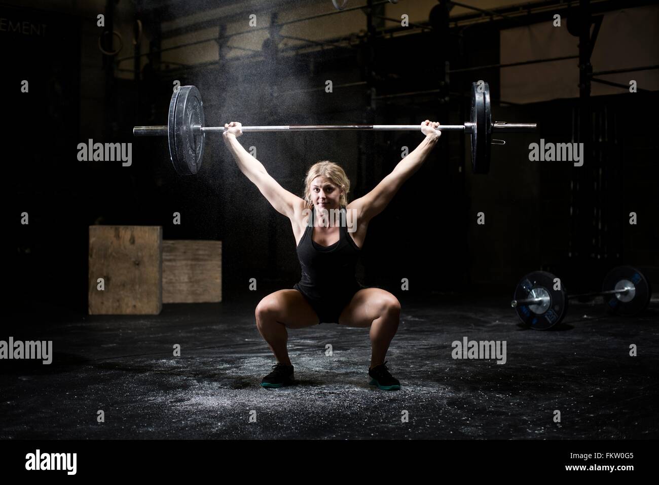 Young woman weightlifting barbell in dark gym Stock Photo