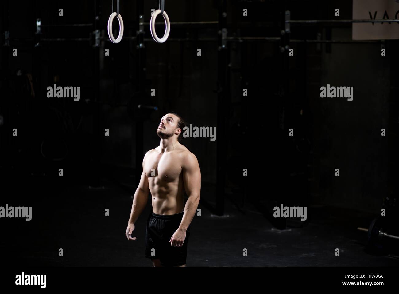Bare chested young man preparing to use gym rings in dark gym Stock Photo