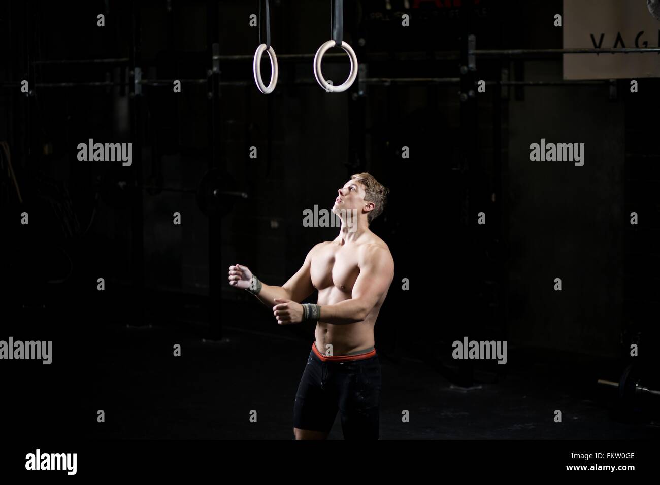 Bare chested young man preparing to use gym rings in dark gym Stock Photo