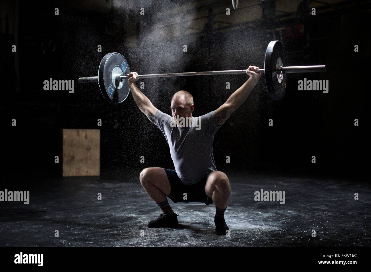 Young man weightlifting barbell in dark gym Stock Photo