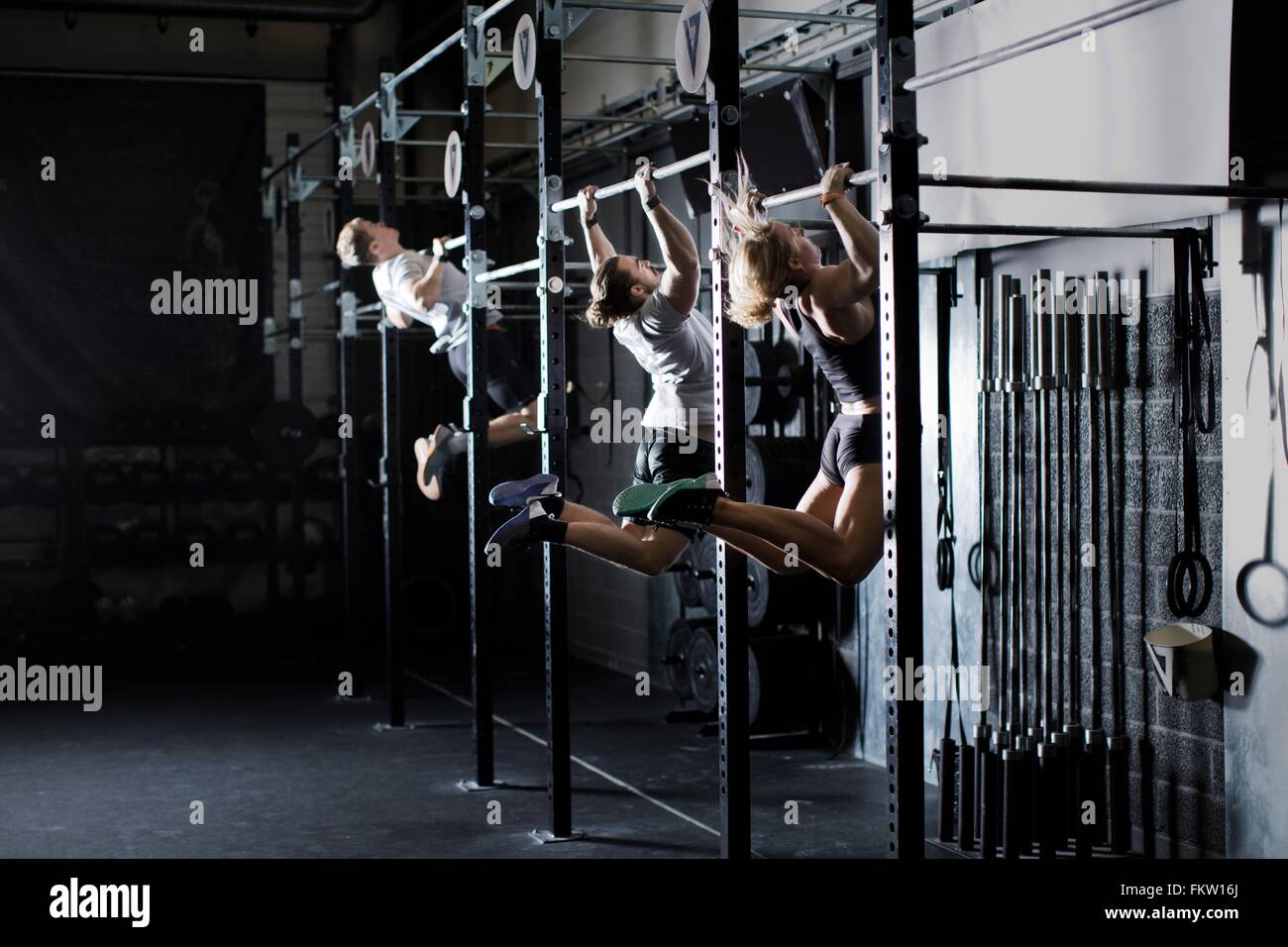 Three young adults training on wall bar in gym Stock Photo