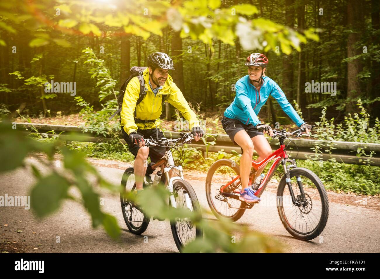 Mature mountain biking couple cycling along rural forest road Stock Photo