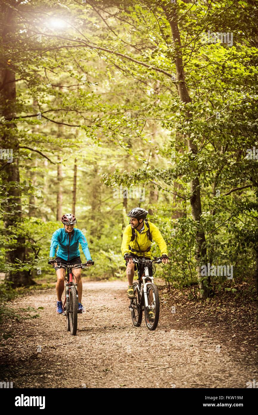 Mature mountain biking couple chatting and cycling on forest trail Stock Photo