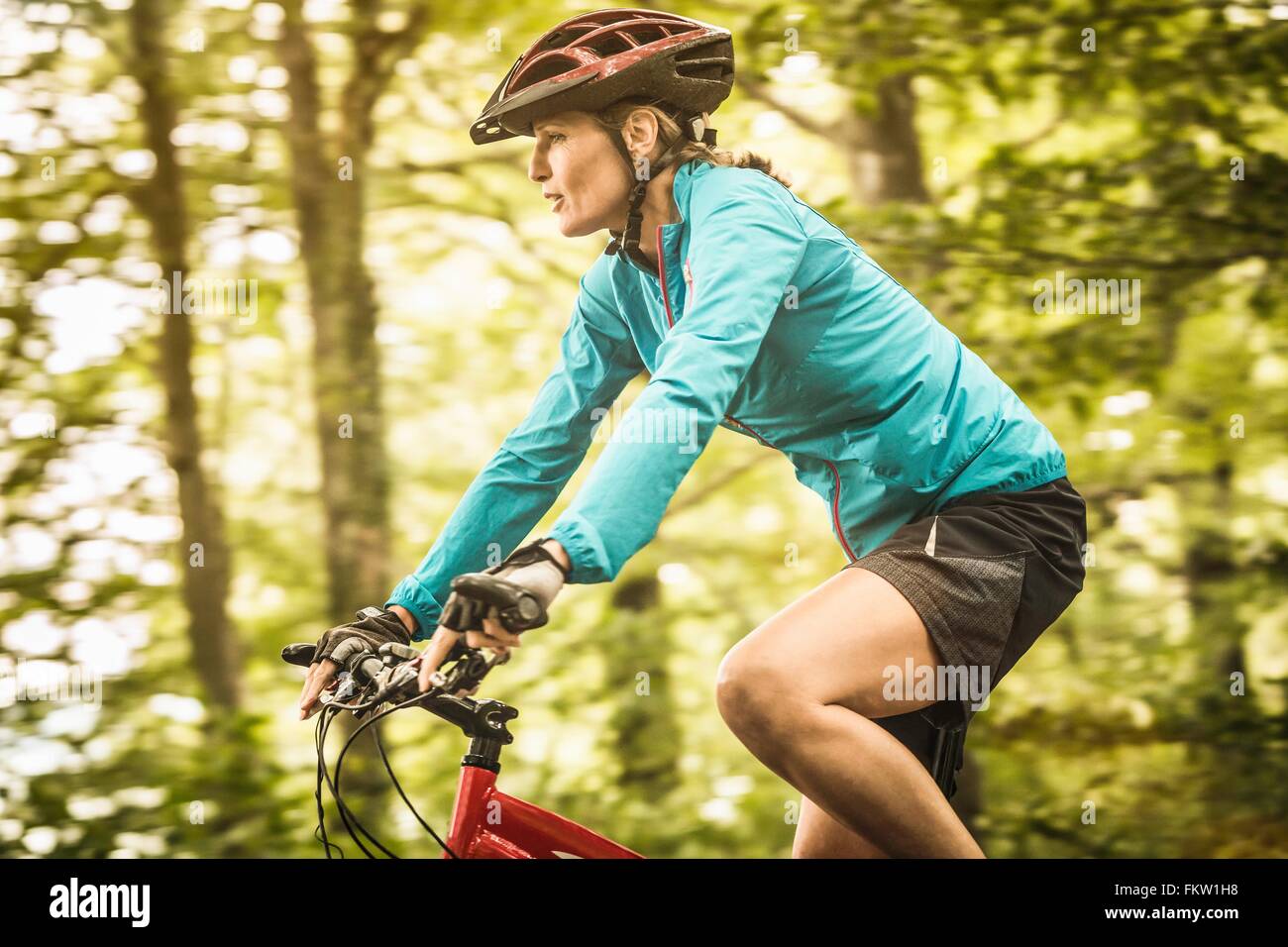 Happy mature female mountain biker speed cycling in forest Stock Photo