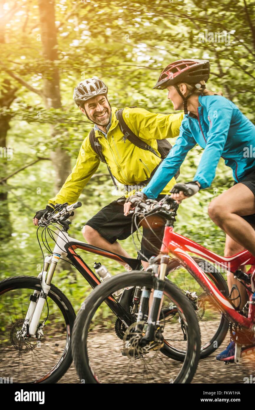 Mature mountain biking couple chatting and cycling along rural forest trail Stock Photo