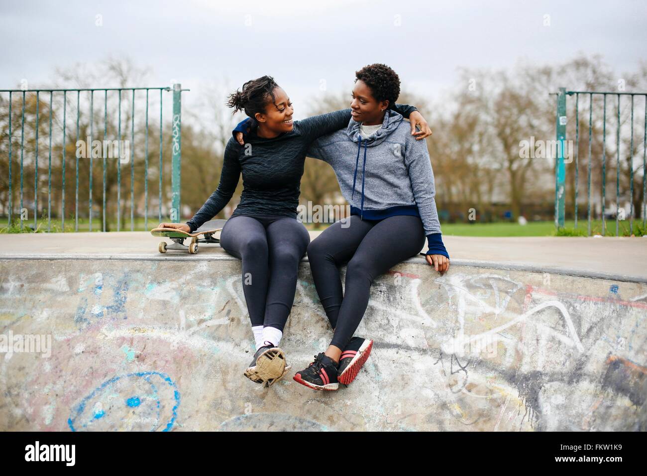 Two young female skateboarding friends sitting in skateboard park Stock Photo