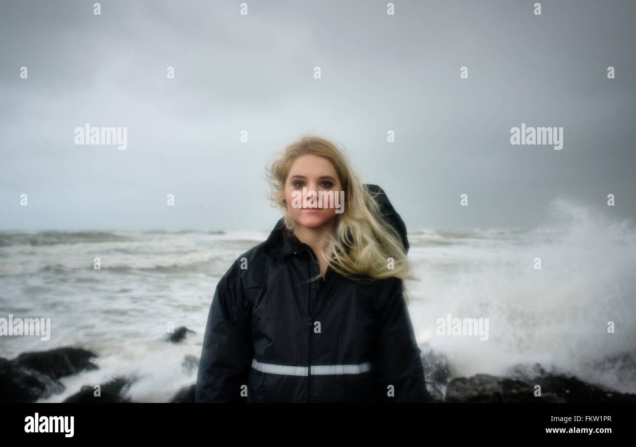 Portrait of young woman with smudged mascara standing in front of splashing ocean waves Stock Photo