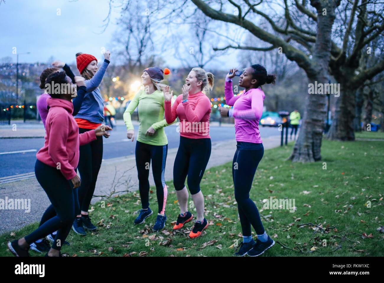 Six female adult runners celebrating on city verge at dusk Stock Photo
