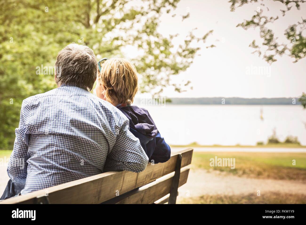 Rear view of adult couple on lakeside park bench Stock Photo