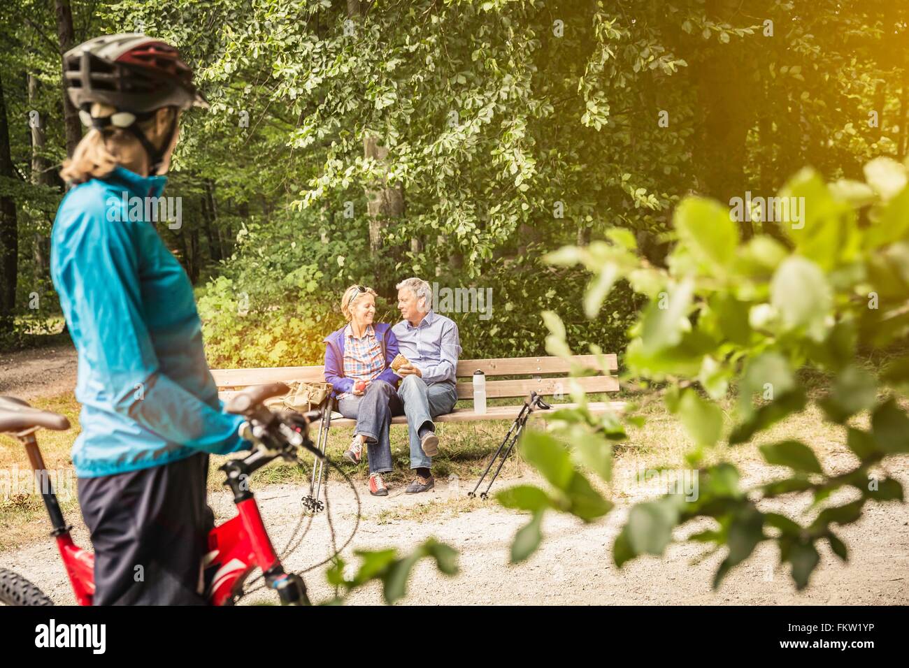 Female mountain biker watching happy couple on park bench Stock Photo