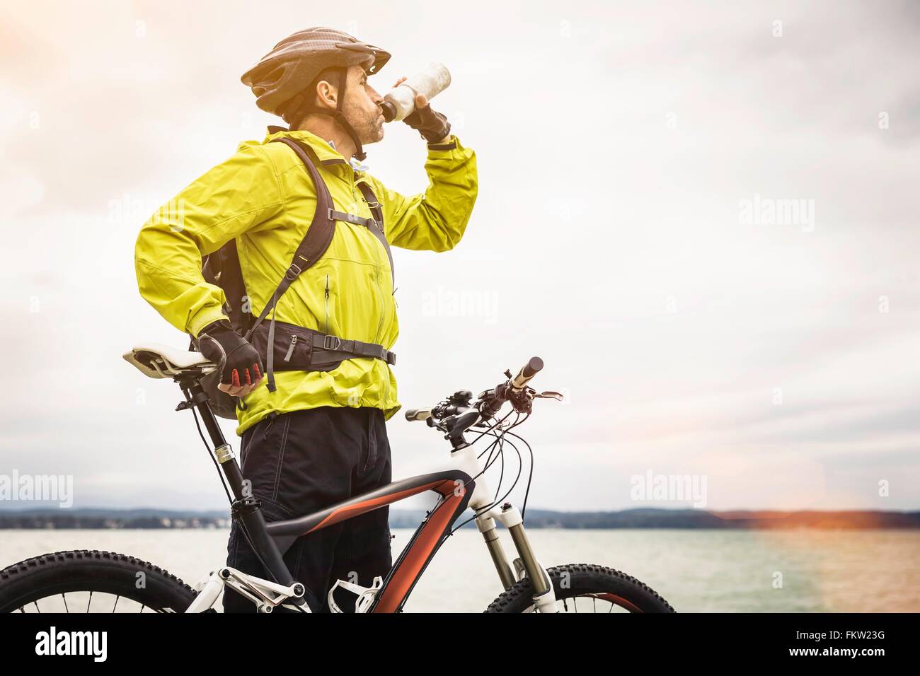 Mature male mountain biker drinking water at lakeside Stock Photo