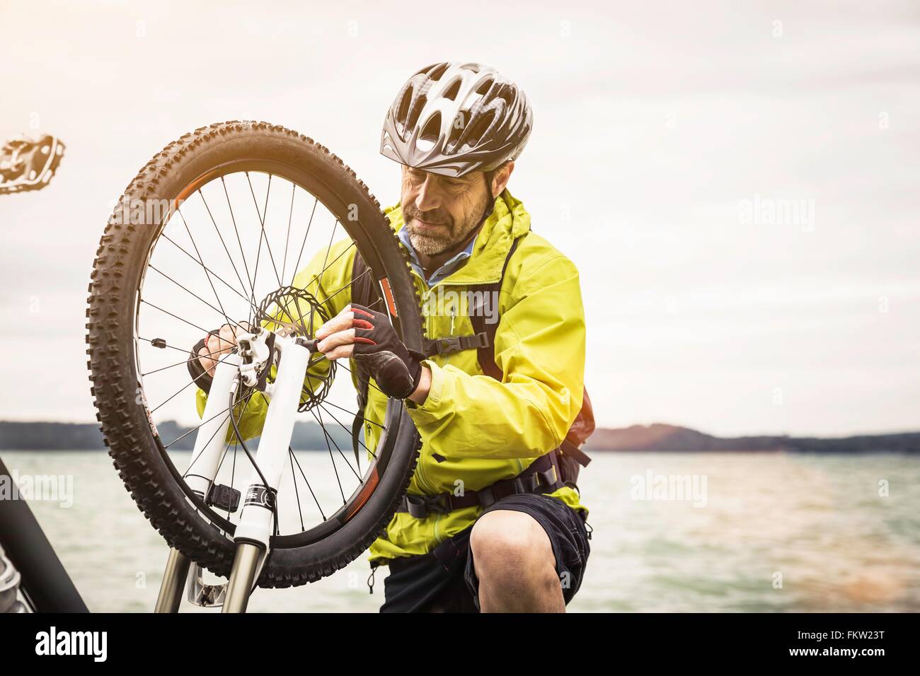 Male mountain biker repairing cycle wheel at lakeside Stock Photo