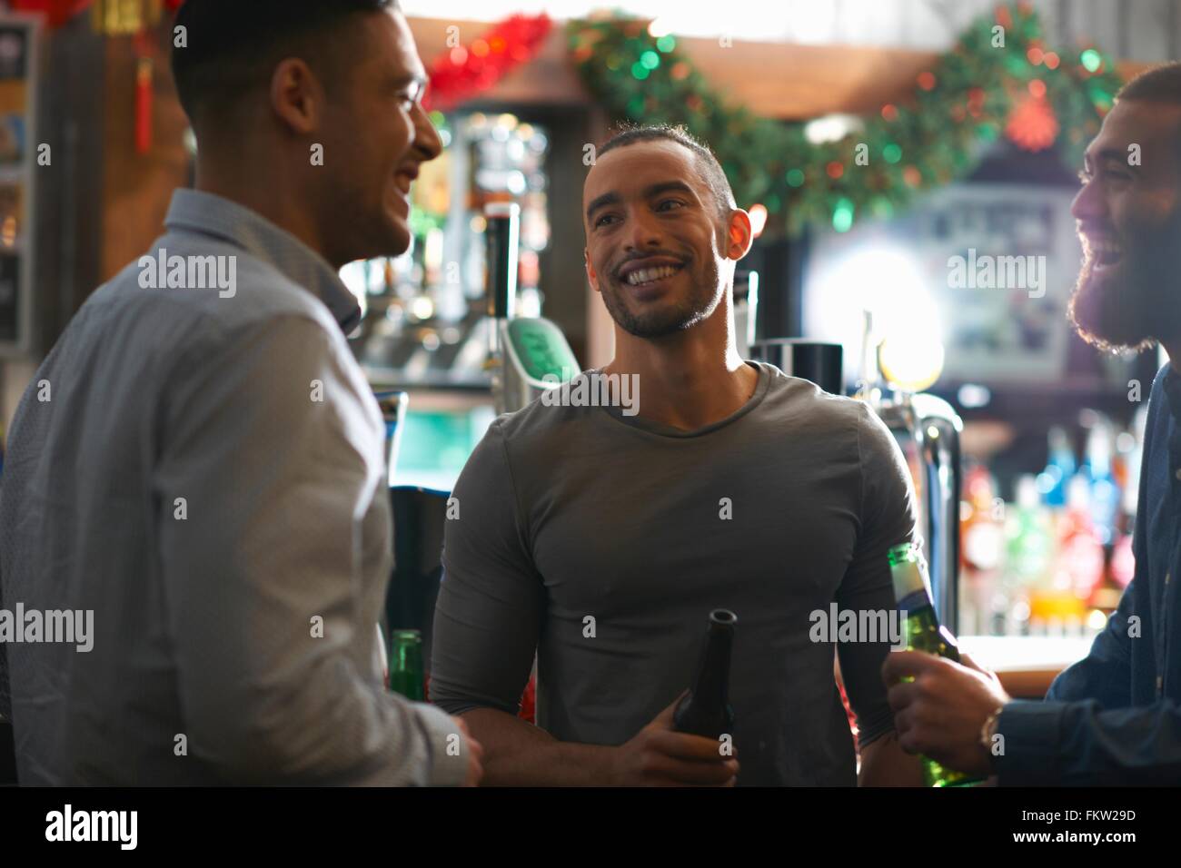 Young man in public house holding beer bottle looking at friend smiling Stock Photo