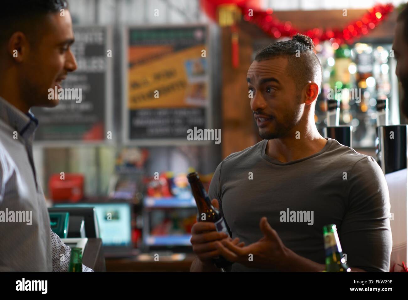 Young man in public house holding beer bottle talking to friend Stock Photo