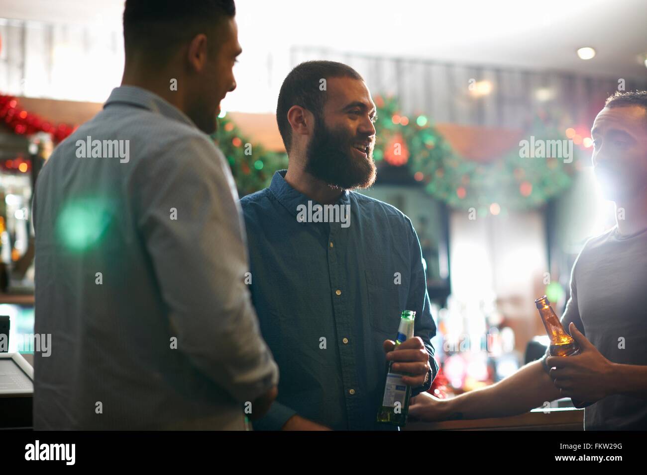Young men in public house holding beer bottles leaning against counter smiling Stock Photo