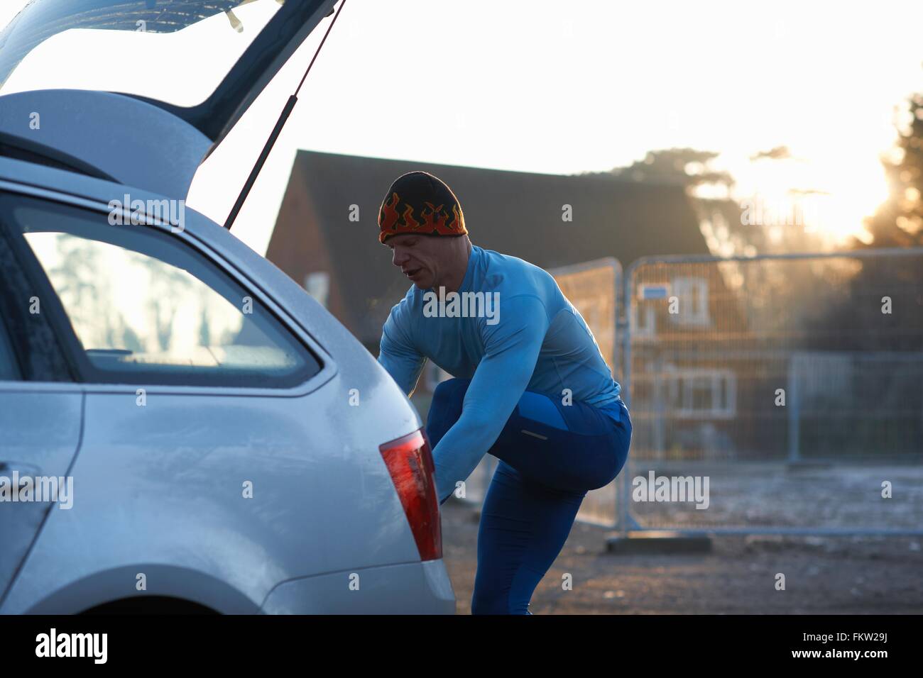 Runner with leg raised on car boot tying shoelace Stock Photo Alamy