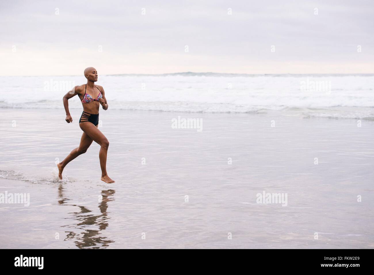 Woman in bikini jogging on beach Stock Photo