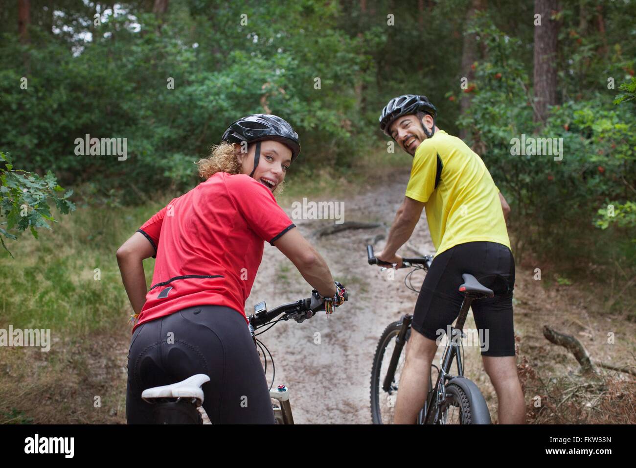 Portrait   mountain biking couple looking over their shoulders in forest Stock Photo