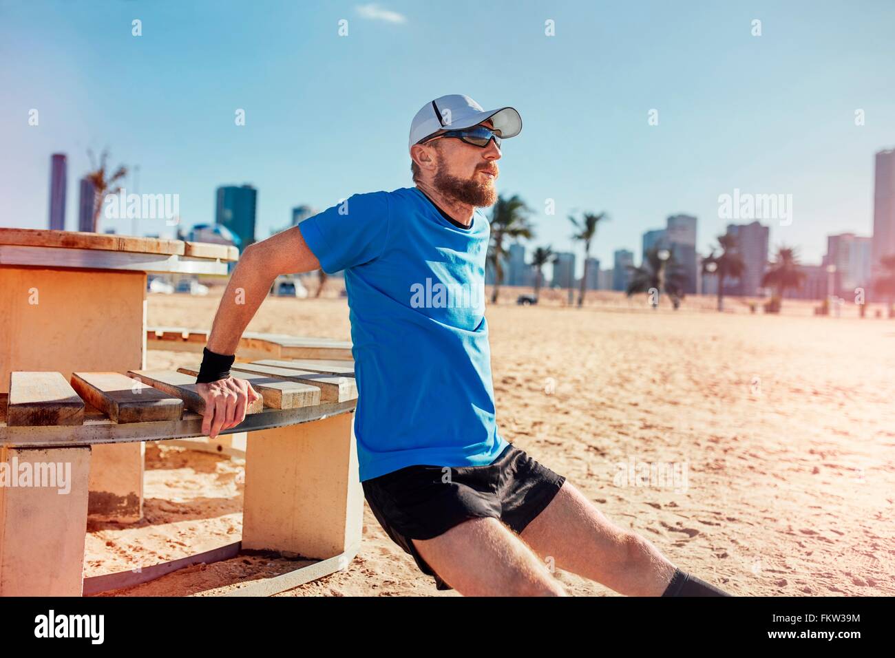 Mid adult man on beach doing reverse push up on bench, Dubai, United Arab Emirates Stock Photo