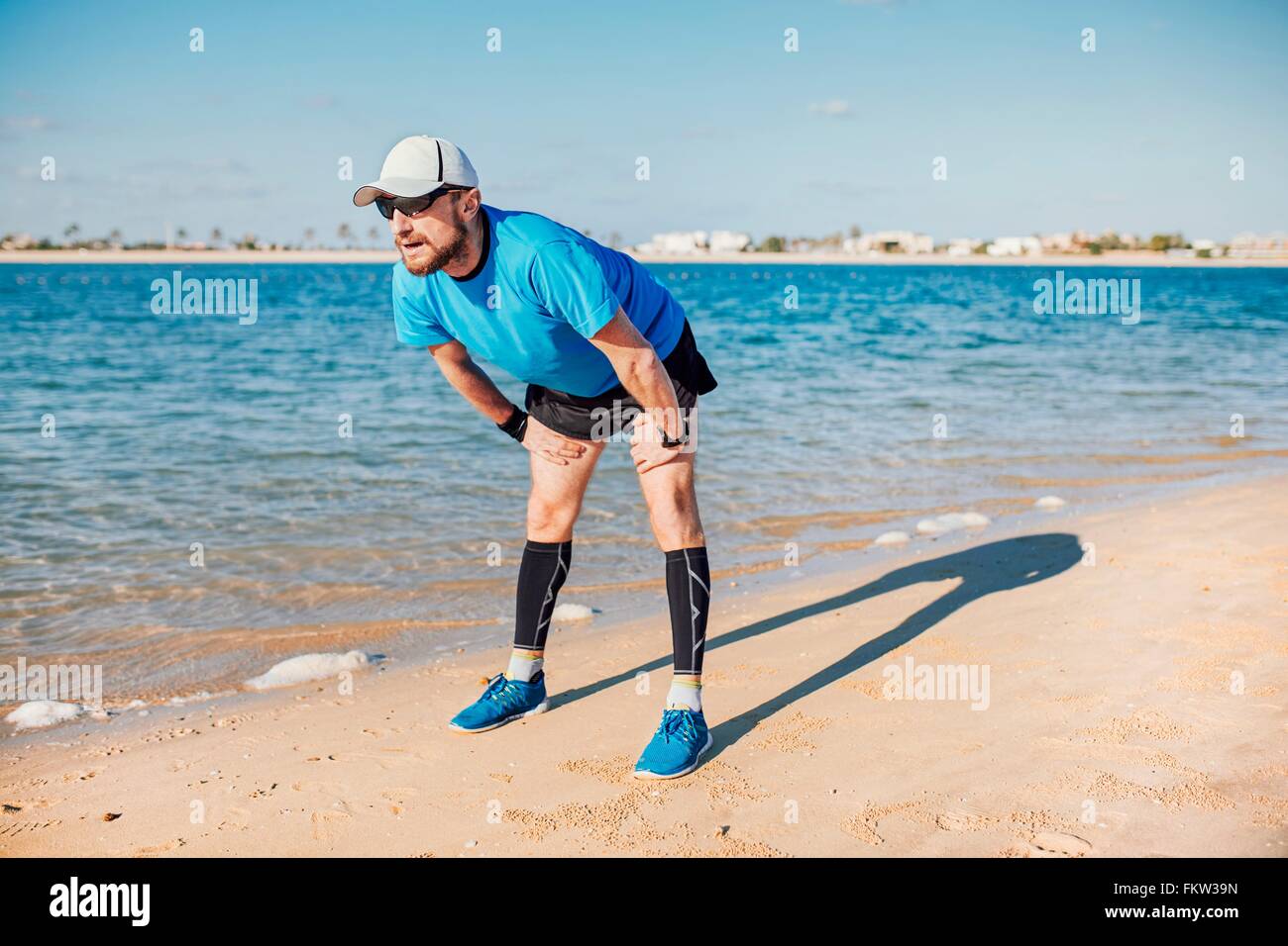 Mid adult man on coastline bending forwards looking away, Dubai, United Arab Emirates Stock Photo