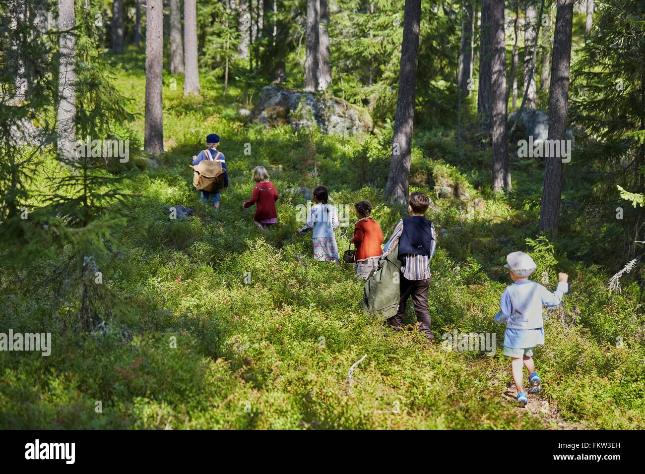Six boys and girls dressed in retro clothing walking in forest Stock Photo