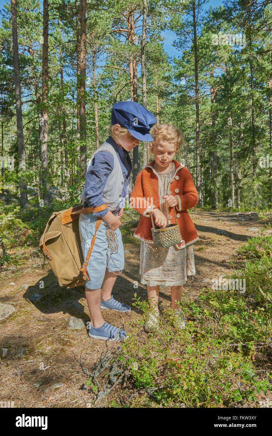 Boy and girl wearing retro clothes picking berries in forest Stock Photo