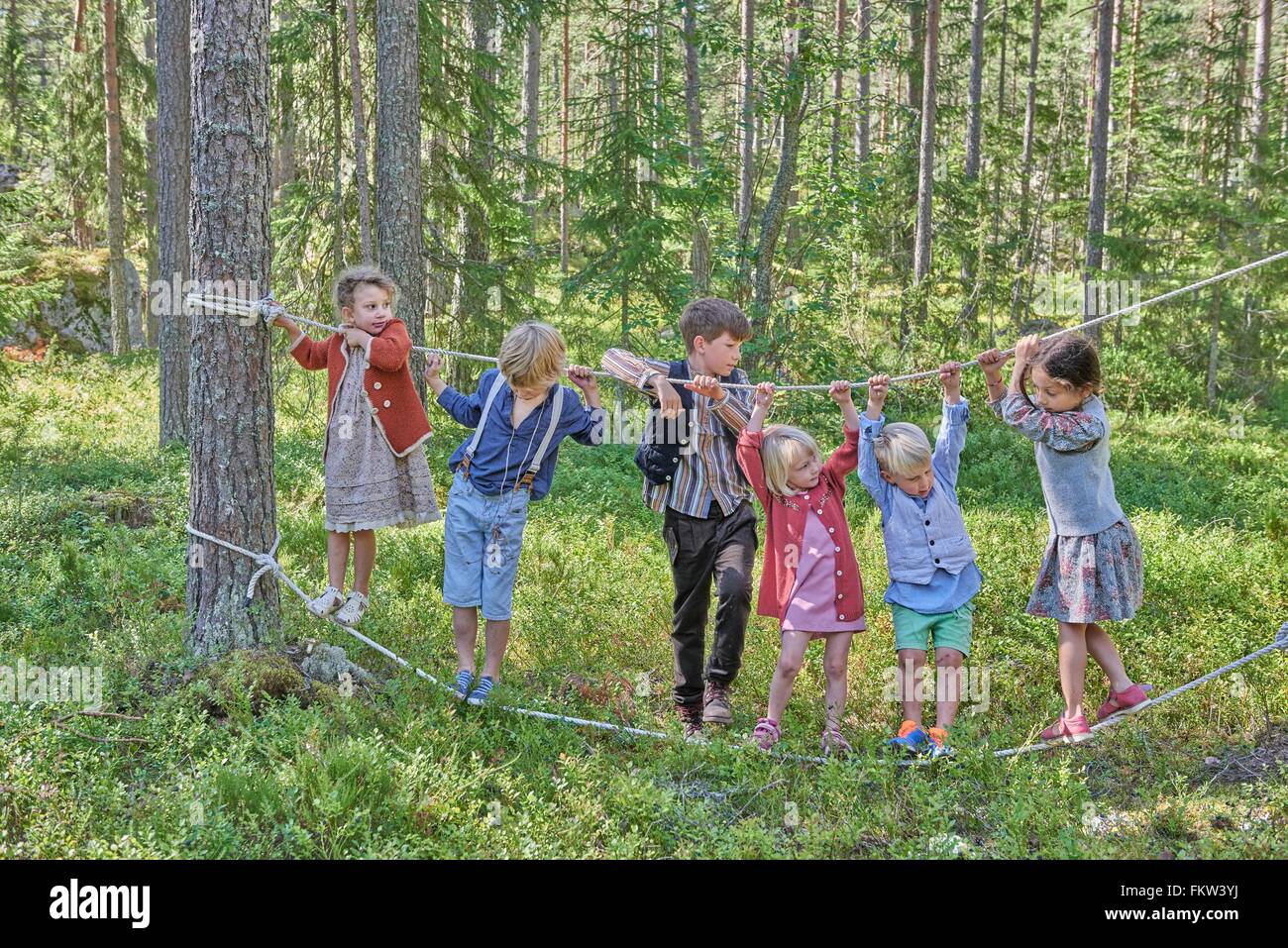 Girls and boys wearing retro clothes balancing on ropes in forest Stock Photo