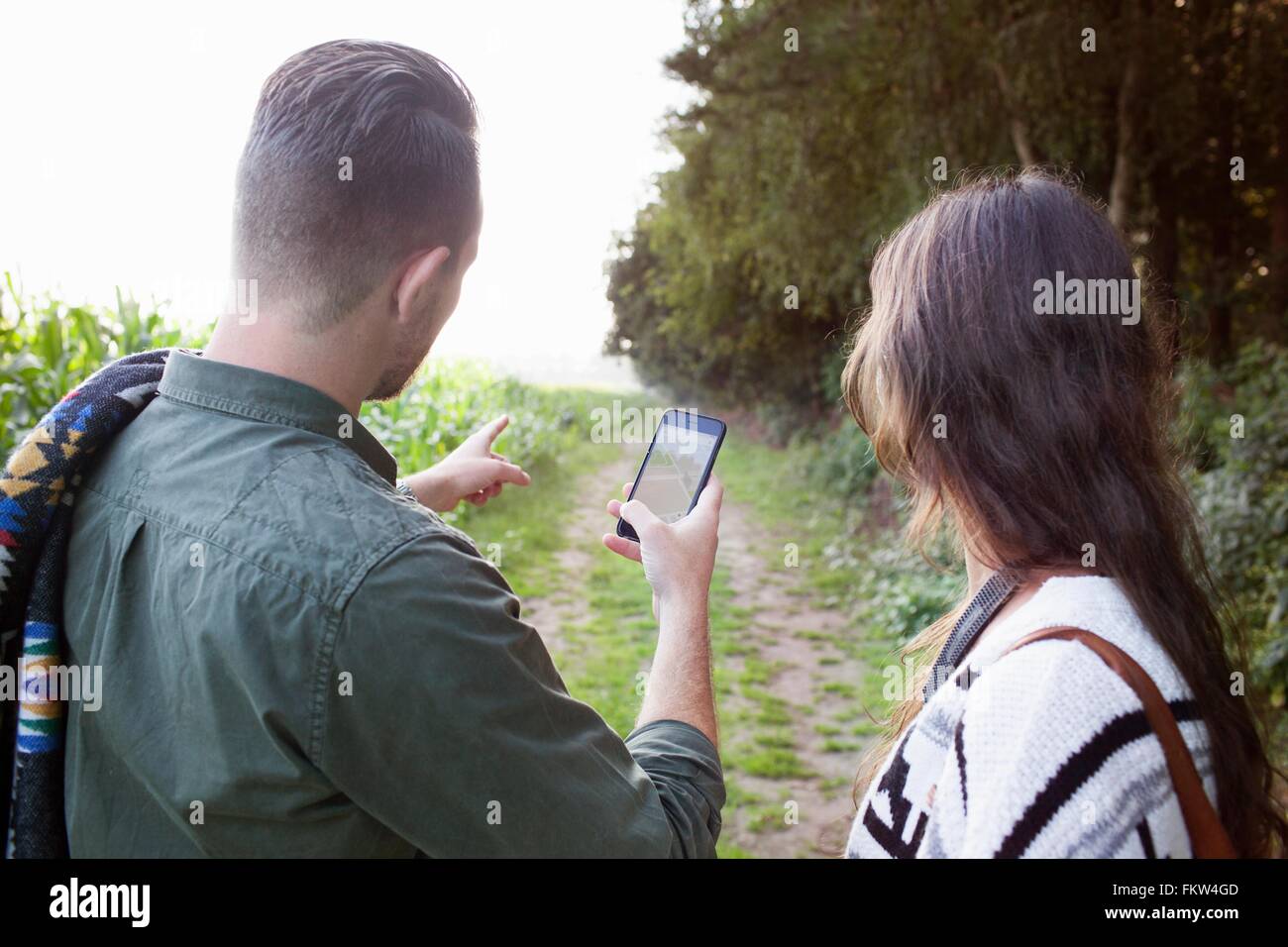 Over shoulder view of couple navigating with smartphone in field Stock Photo