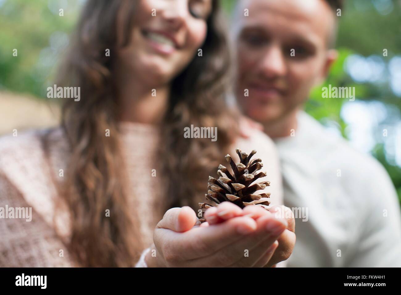 Shallow focus of couple with woman holding pine cone on hand Stock Photo