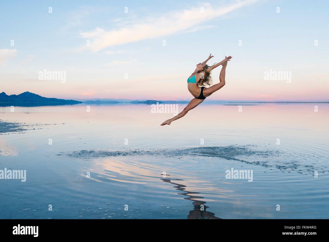 Female ballet dancer leaping mid air over lake, Bonneville Salt Flats, Utah, USA Stock Photo