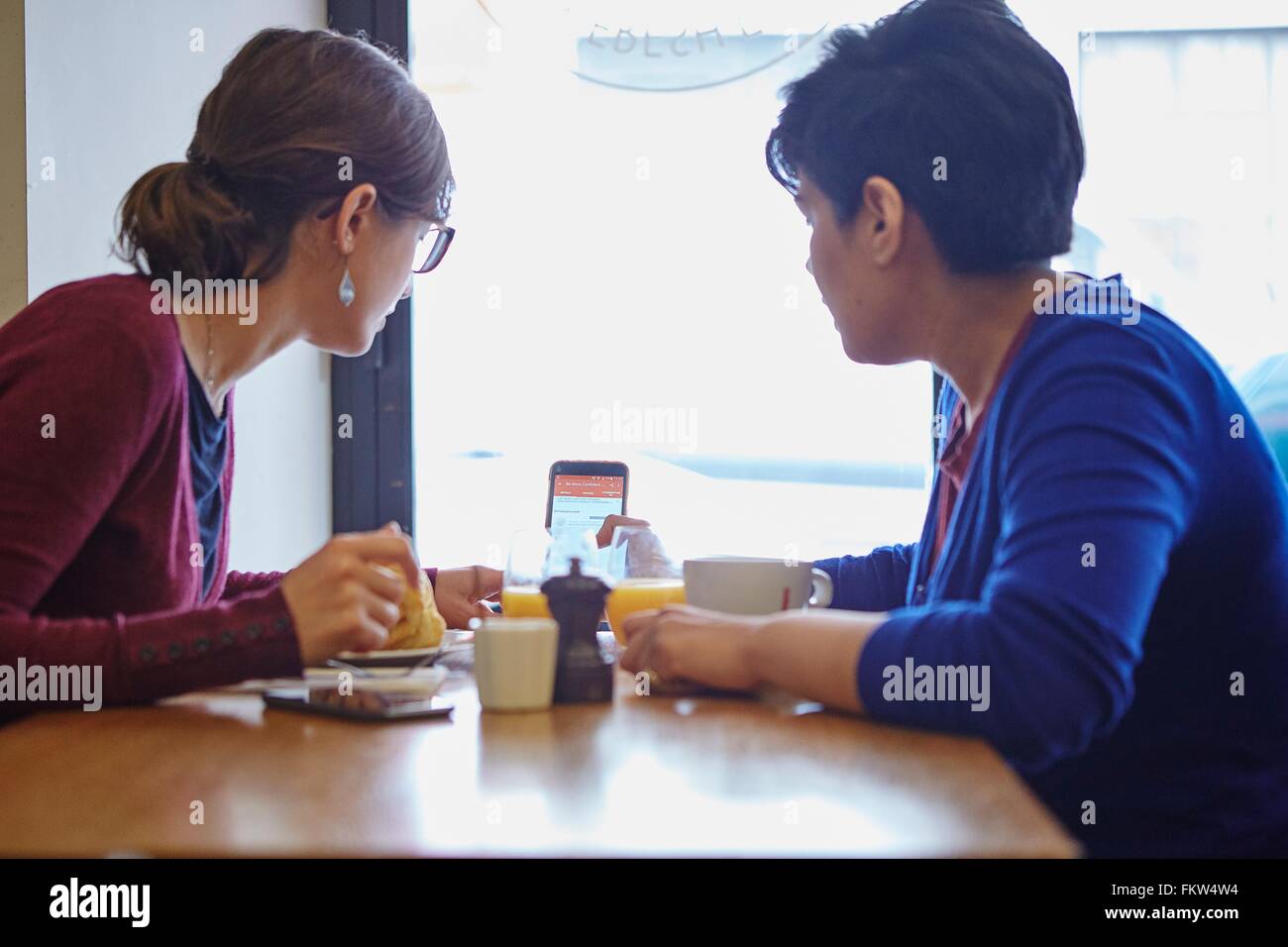 Two women reading smartphone text in restaurant Stock Photo