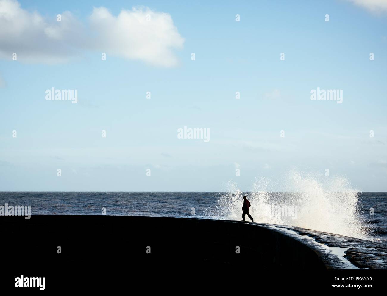 Person running away from splashing wave on 'The Cobb' harbour wall, Lyme Regis, Dorset, England Stock Photo