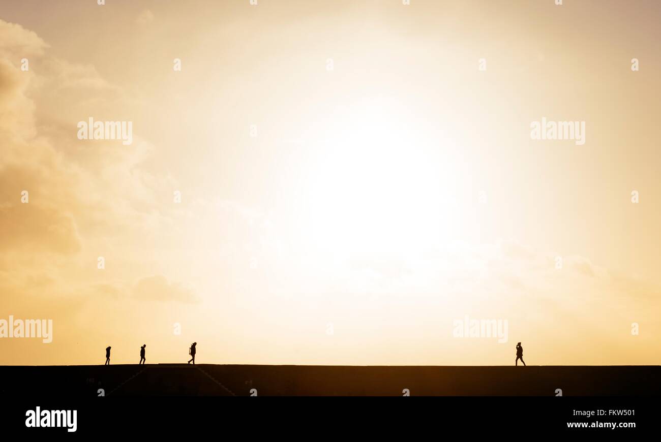 Silhouetted view of people strolling on 'The Cobb' harbour wall at sunset, Lyme Regis, Dorset, England Stock Photo