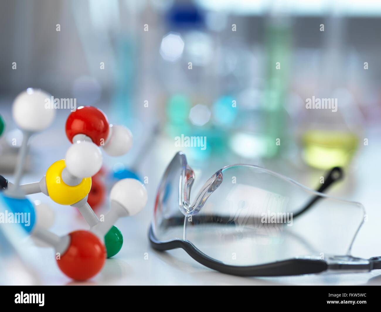 Safety glasses and molecular model on laboratory bench Stock Photo