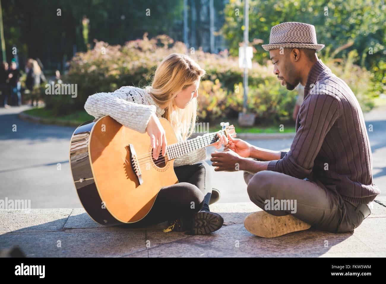 Couple learning to play guitar in park Stock Photo