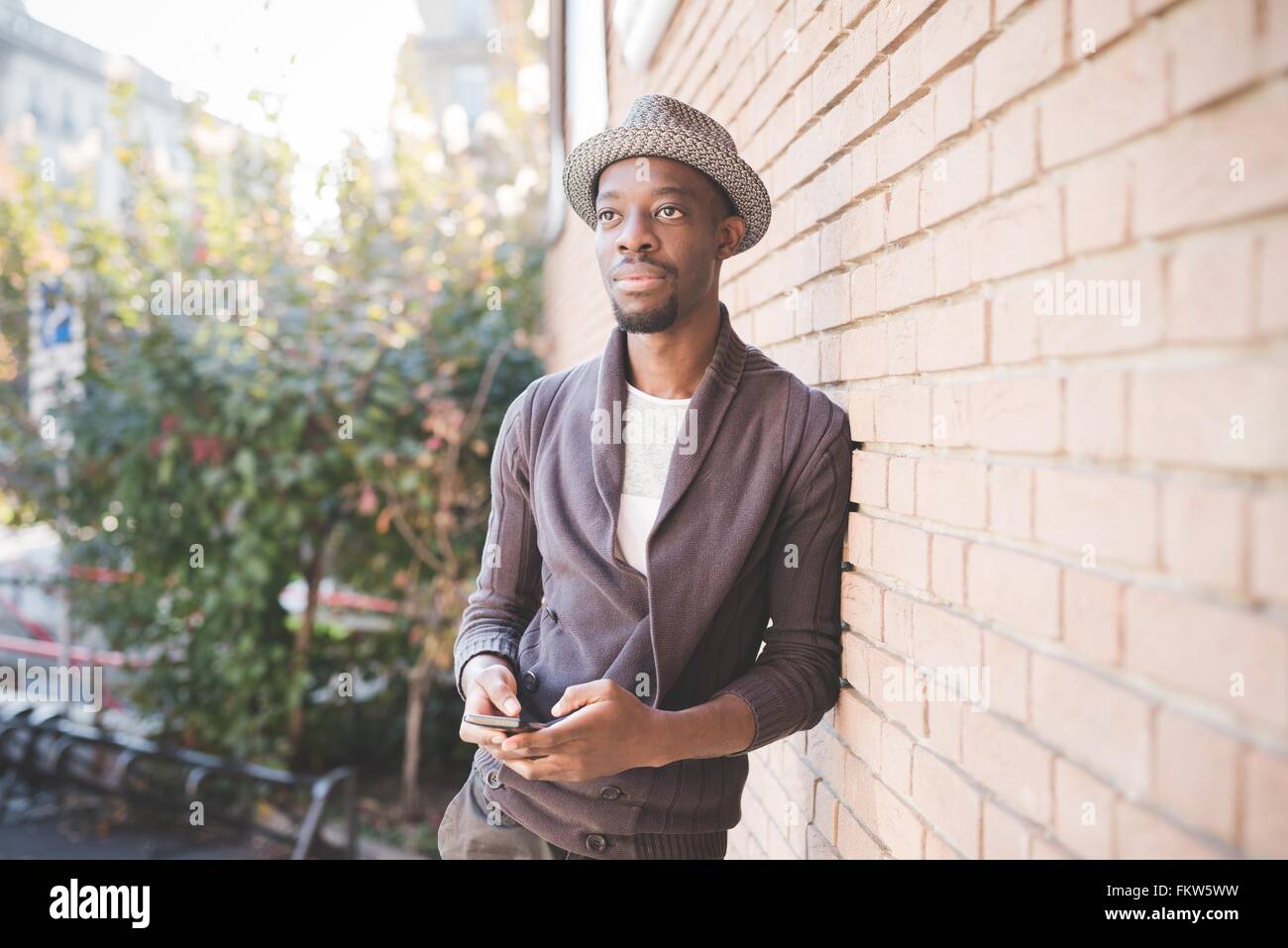 Man with smartphone leaning against brick wall Stock Photo - Alamy
