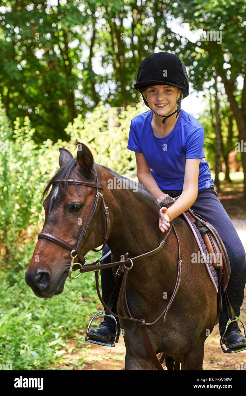 Girl on horse wearing riding hat looking at camera smiling Stock Photo