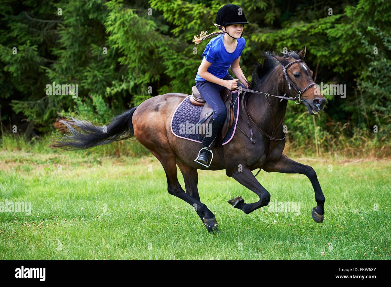 Side view of girl wearing riding hat galloping on horseback Stock Photo