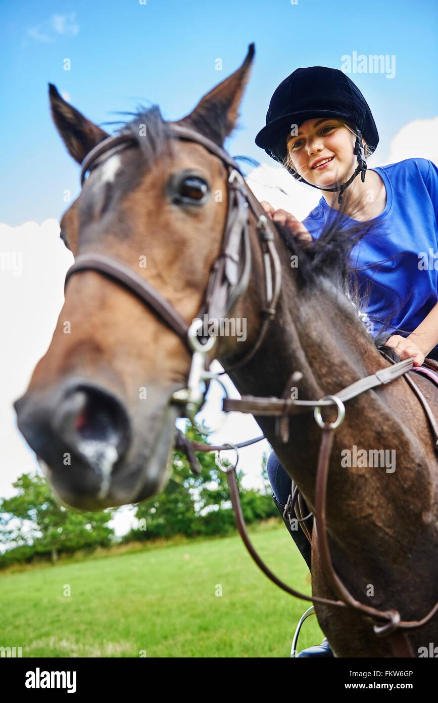 Low angle view of girl on horseback wearing riding hat smiling Stock Photo