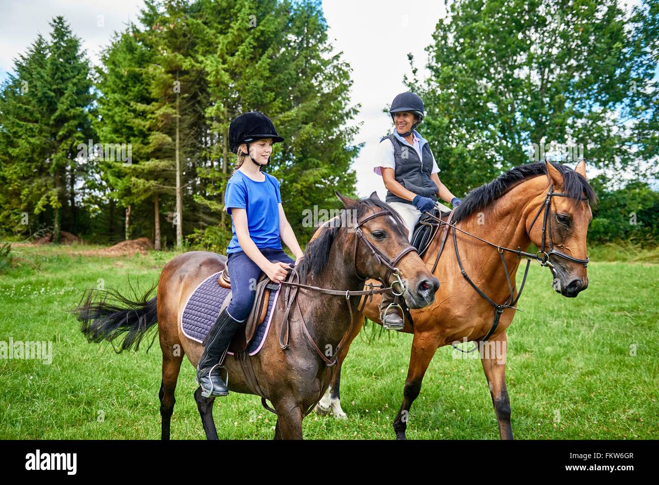 Mature woman and girl on horseback wearing riding hats smiling Stock Photo