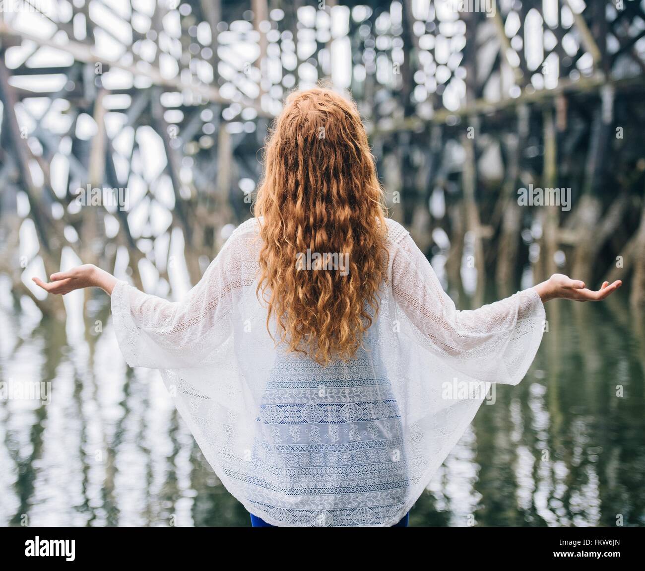 Rear view of woman with long red hair meditating in front of wood river pier Stock Photo