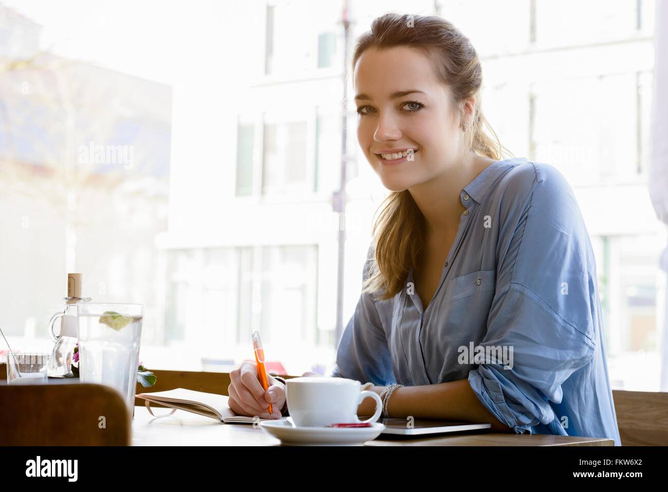 Young woman in cafe writing, looking at camera smiling Stock Photo