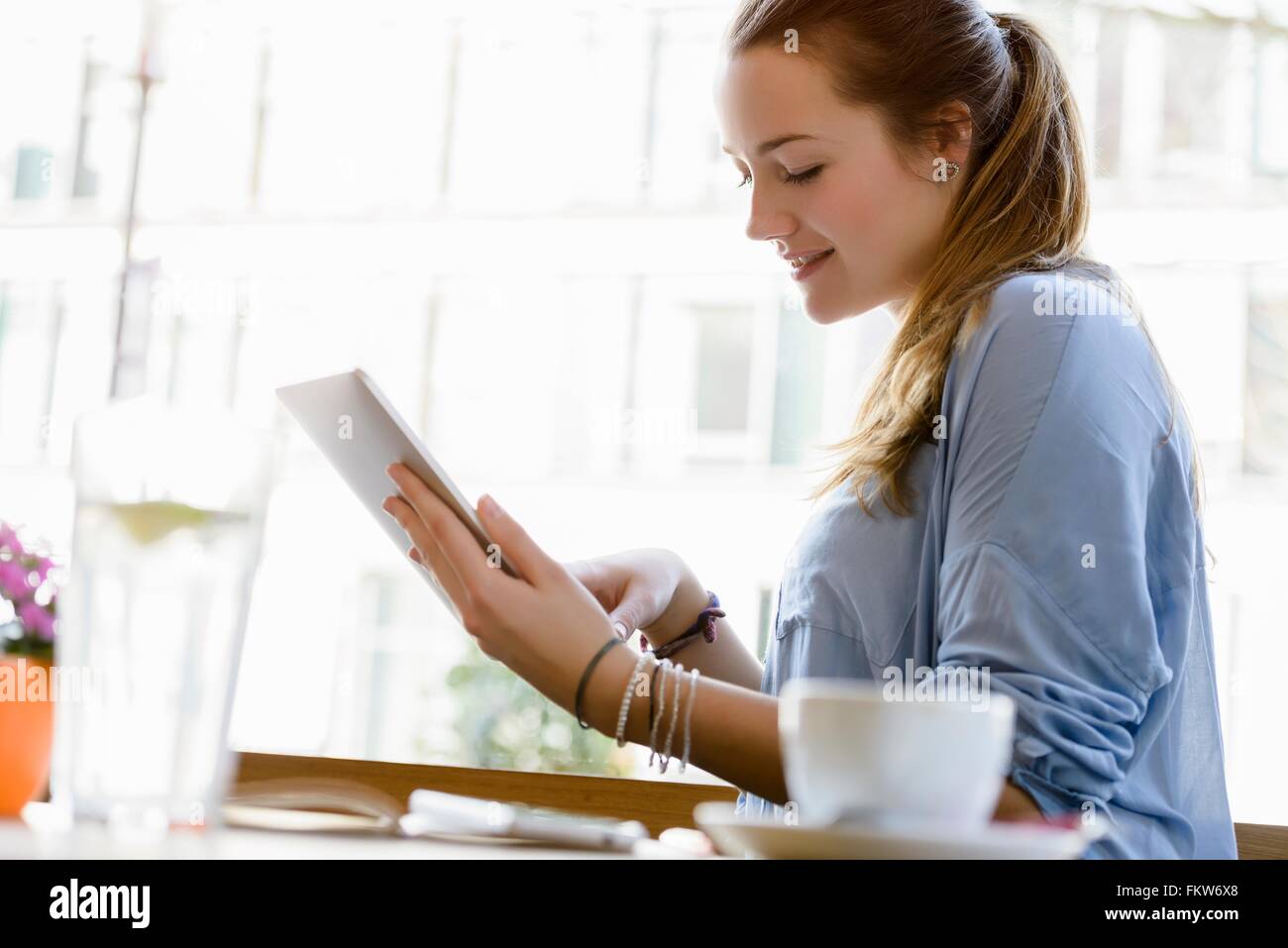Side view of young woman in cafe looking down using digital tablet Stock Photo