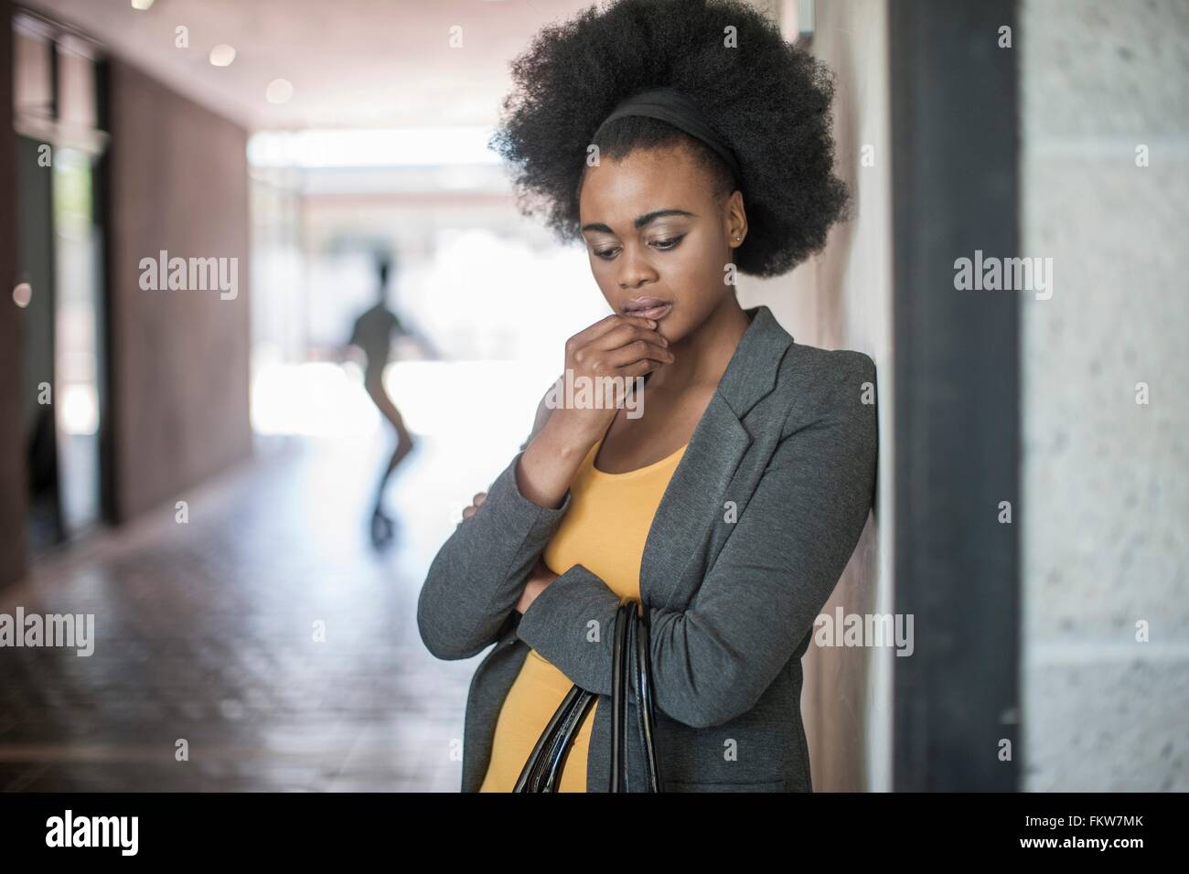 Young businesswomen with hand on chin leaning against office wall Stock Photo
